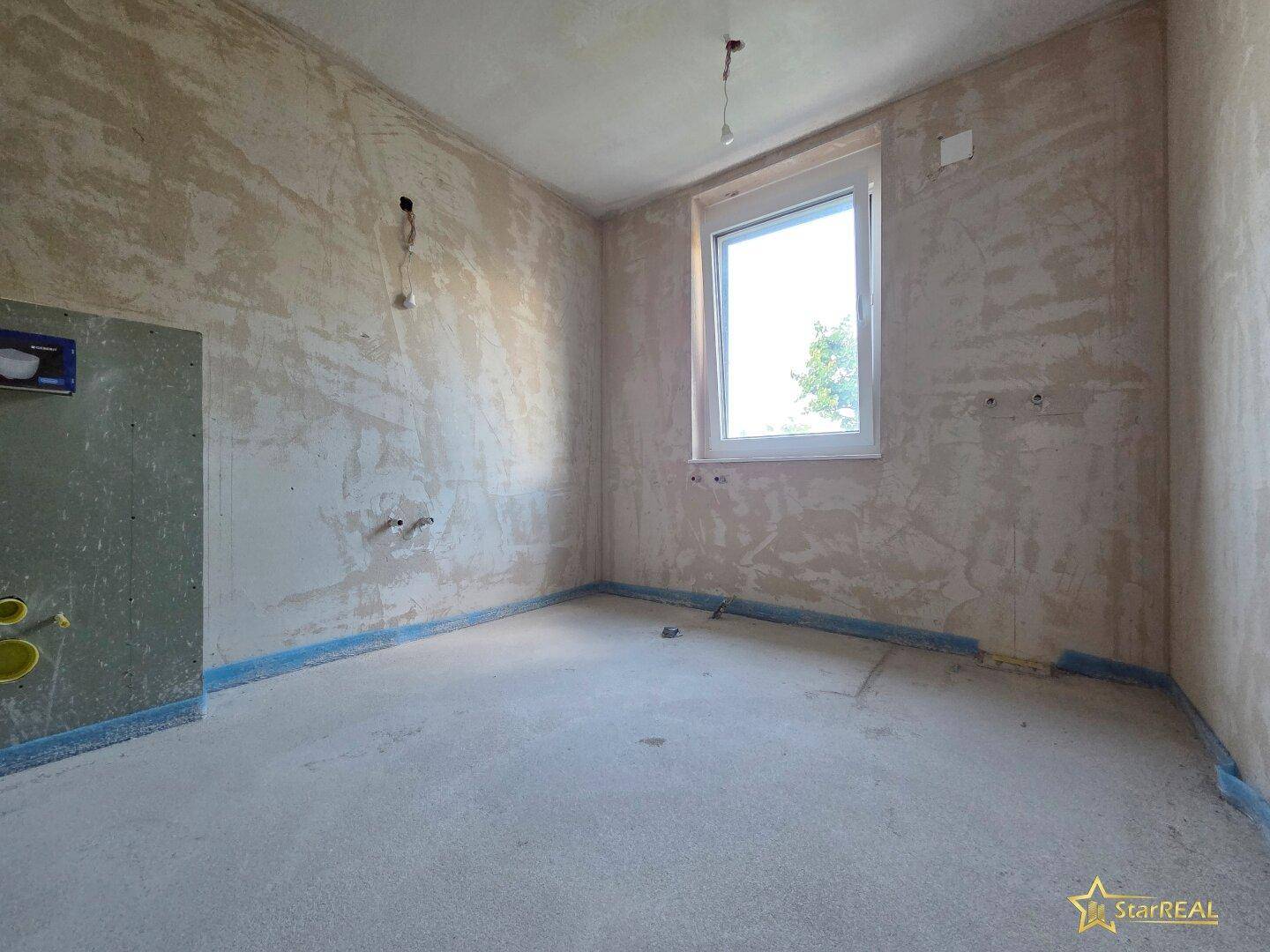 Unfertiges Badezimmer im Rohbauzustand mit sichtbaren Installationen und Fenster.