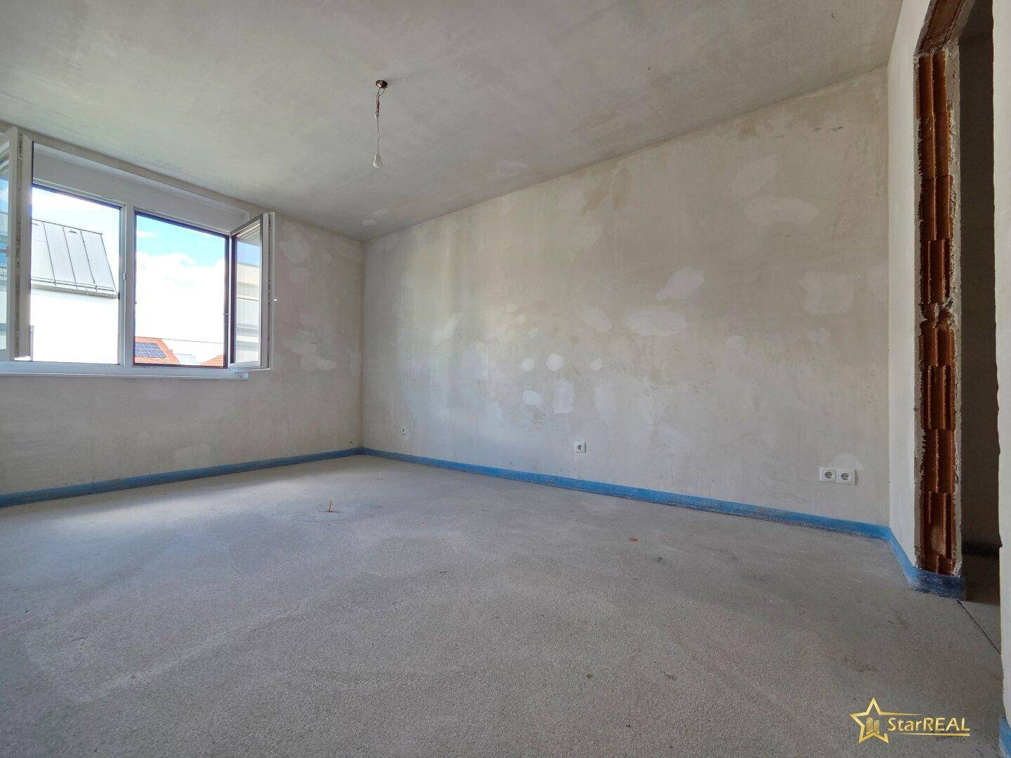 Geräumiges, unfertiges Zimmer mit Fenster, bereit für den Innenausbau.
