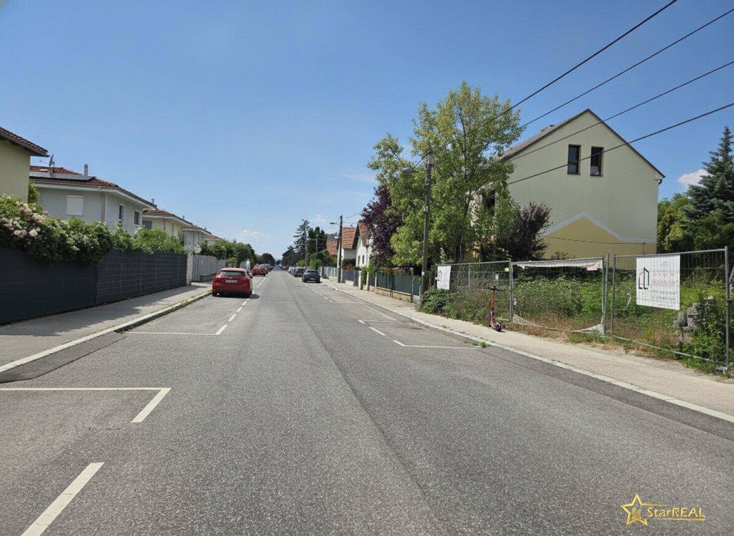 Weitläufige Straßenansicht einer ruhigen Wohngegend mit Einfamilienhäusern unter blauem Himmel.