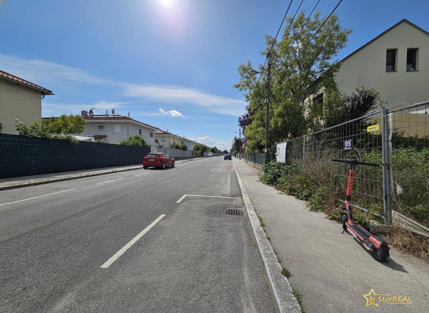 Sonnige Wohnstraße mit gepflegten Häusern und einem unbebauten Grundstück am Straßenrand.