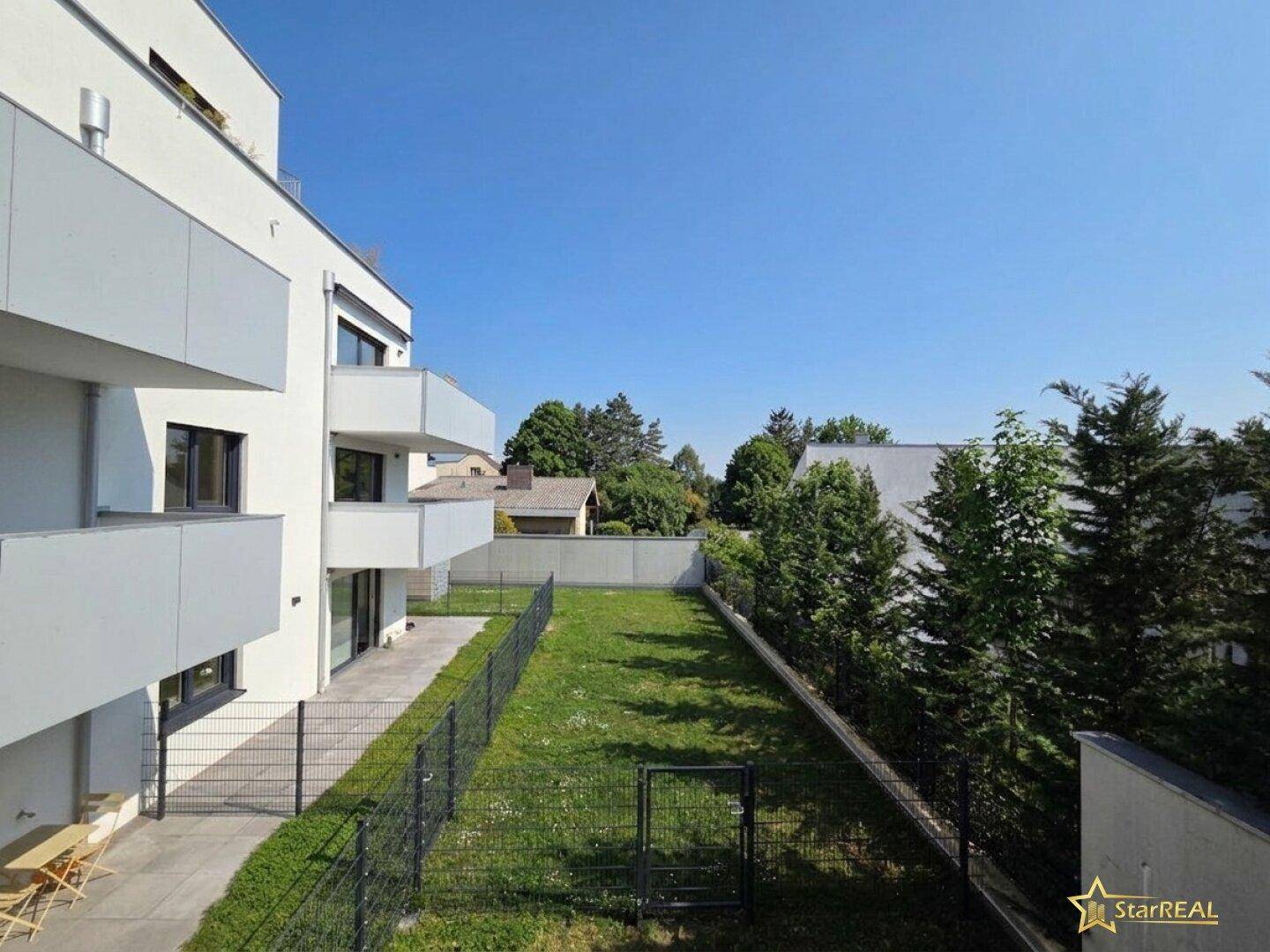 Moderner Neubau mit Balkonen, einer Terrasse im Erdgeschoss und einer gepflegten Rasenfläche.