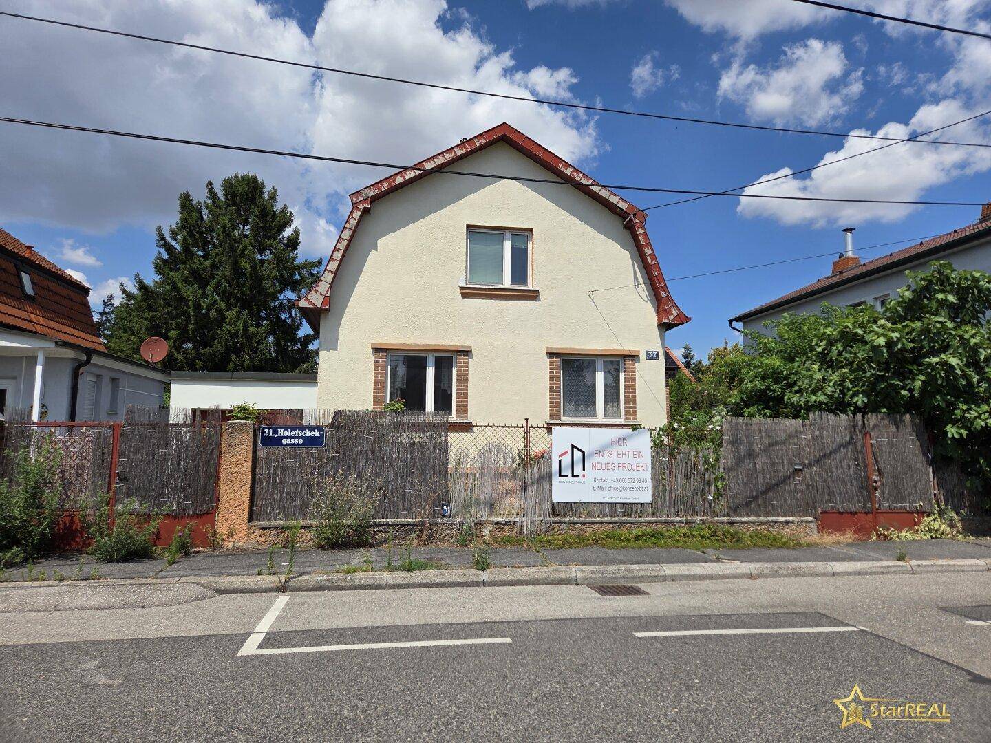 Vorderansicht eines Einfamilienhauses mit heller Fassade, Satteldach und einem Zaun zur Straße.
