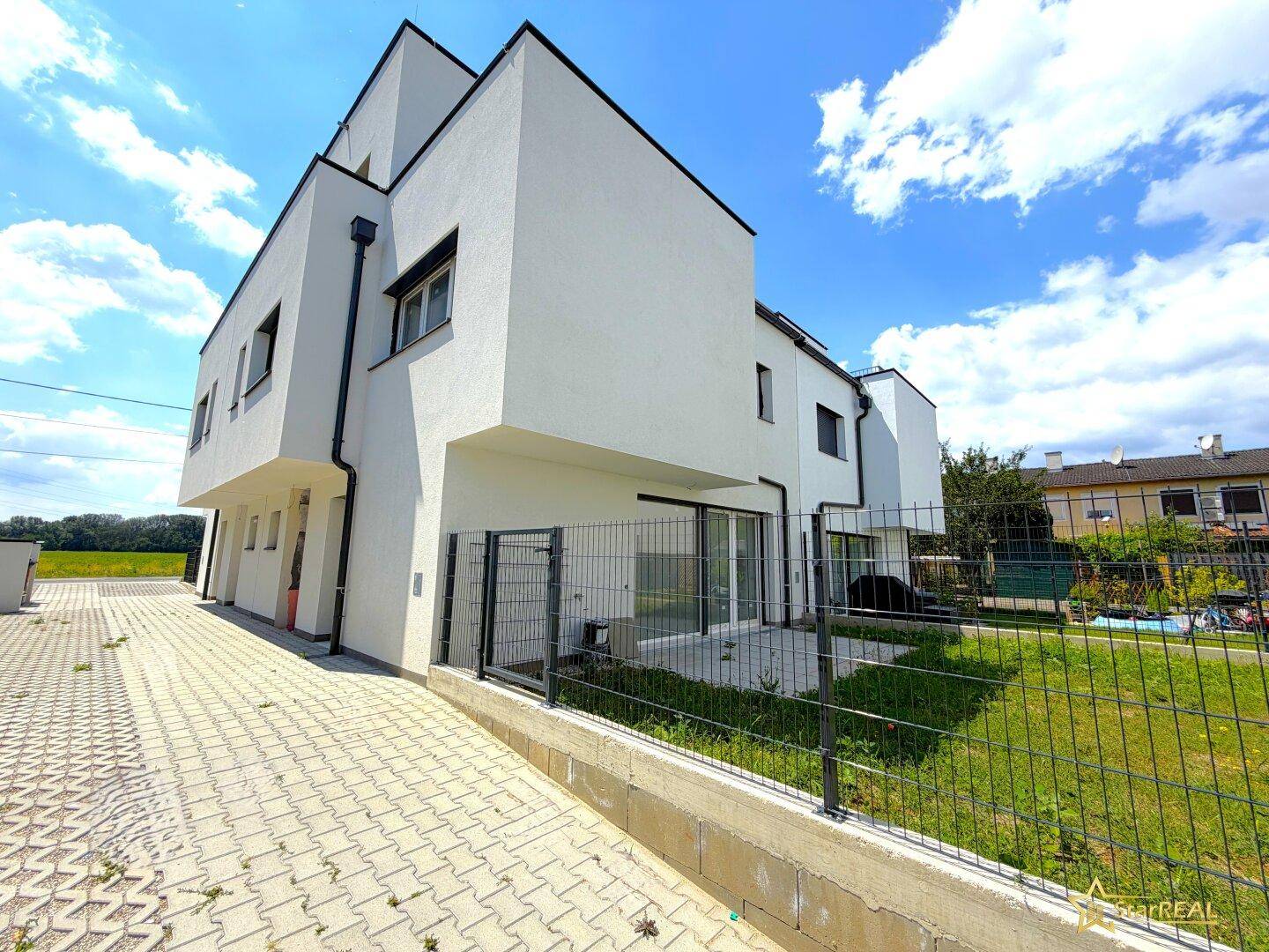 Moderne Reihenhäuser mit weißer Fassade und kleinen Gärten, umgeben von einer ruhigen Wohngegend.