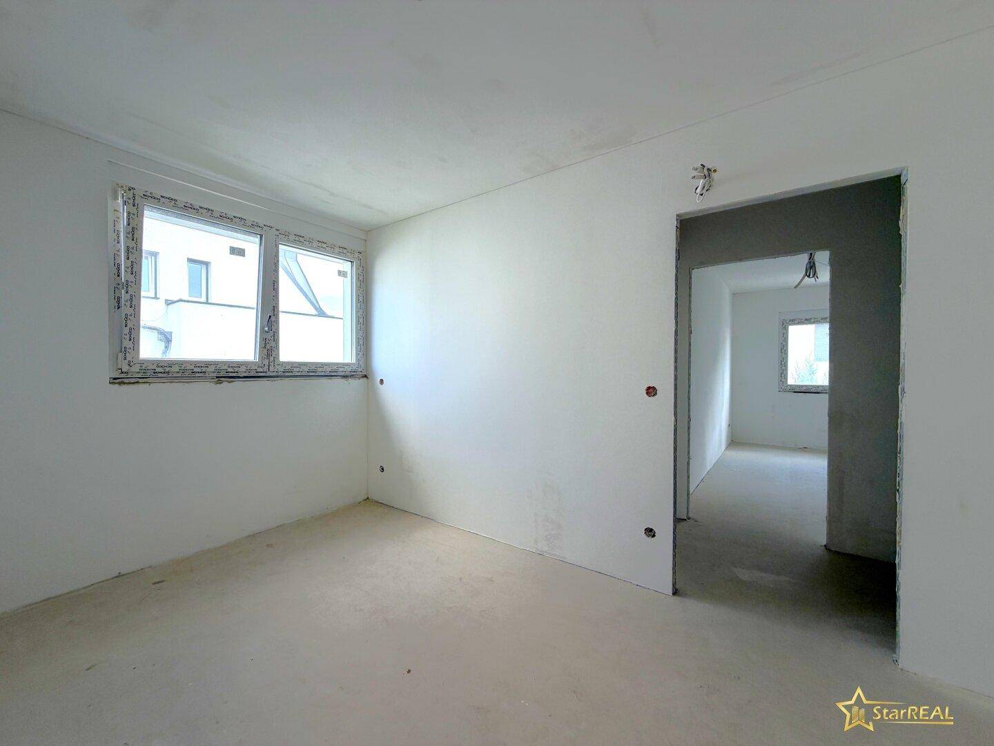 Unfertiger Raum mit weißen Wänden und einem Fenster, bereit für den Innenausbau.
