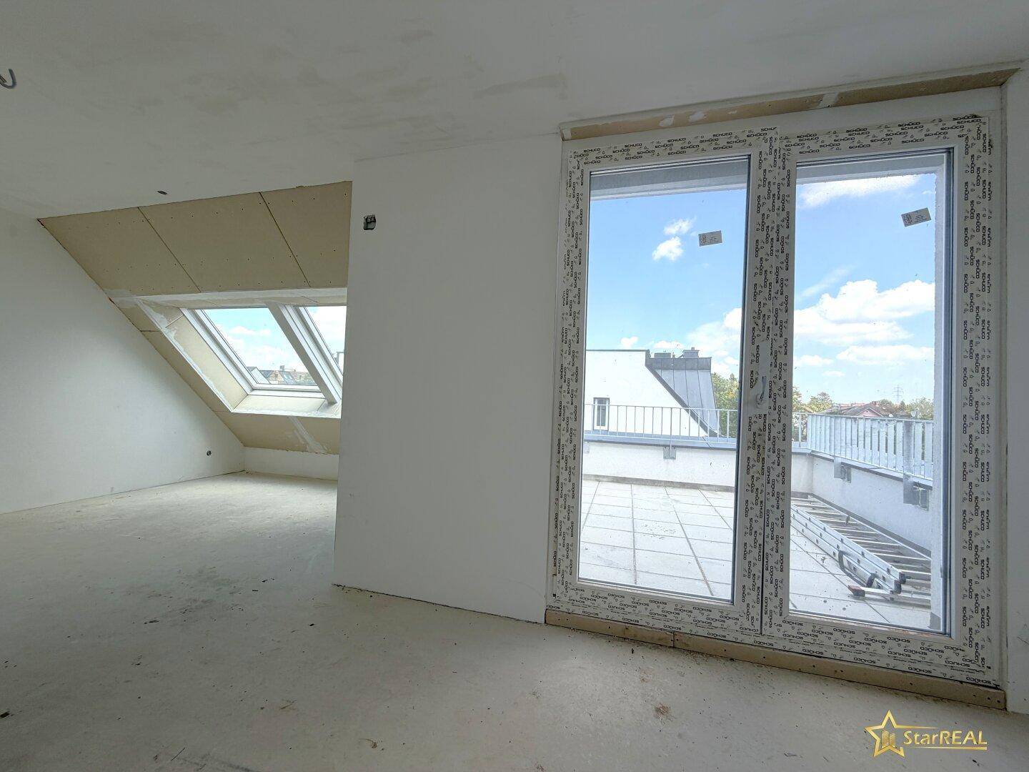 Heller Raum im Dachgeschoss mit Zugang zur Terrasse und Dachfenstern, noch im Rohbau.