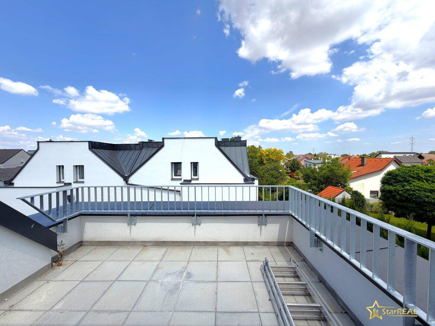 Weitläufige Dachterrasse mit Blick auf die umliegenden Häuser und die grüne Landschaft.