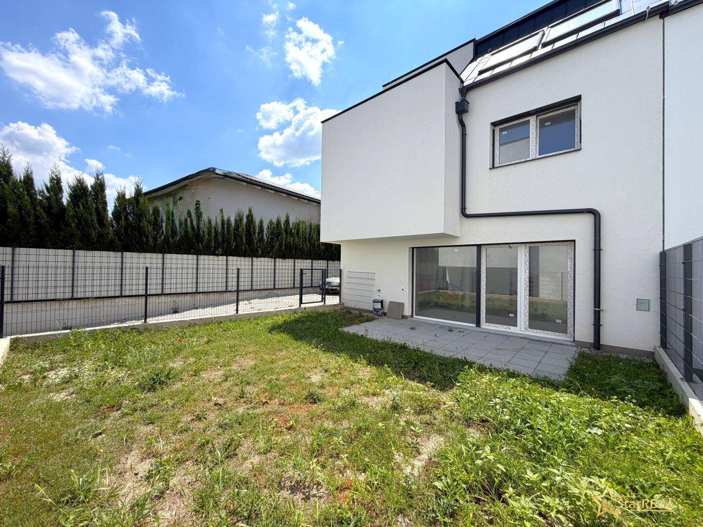 Kleiner Gartenbereich mit Rasenfläche und gepflasterter Terrasse hinter dem Haus.