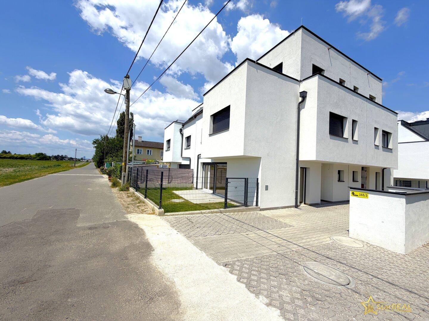 Moderne Reihenhäuser mit weißer Fassade und gepflasterter Zufahrt in einer ruhigen Gegend.