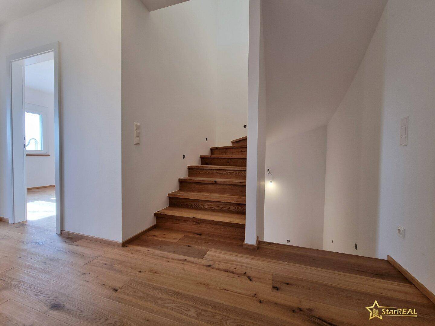 Heller Flur mit Holztreppe und Eichenparkettboden, der zu den oberen Etagen führt.