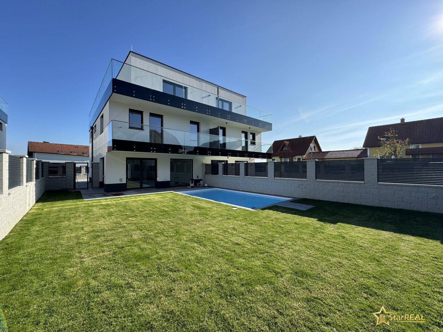 Moderner Neubau mit großem Garten, Pool und Balkonen mit Glasgeländer.