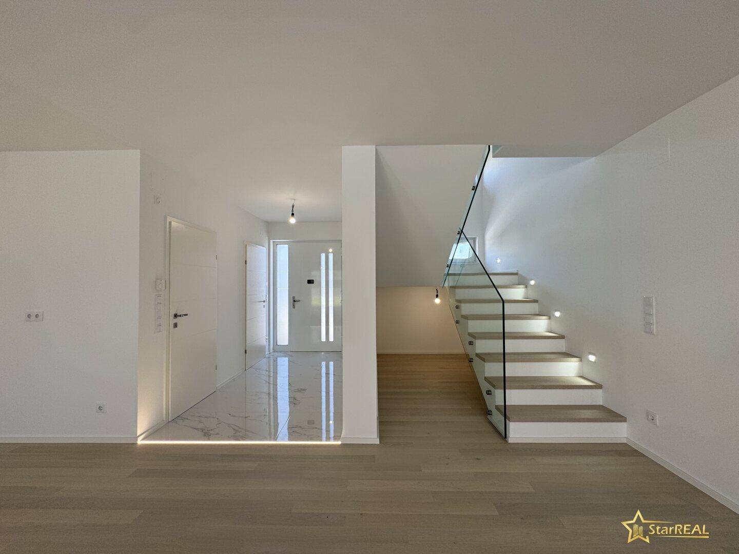 Heller Eingangsbereich mit moderner Treppe, Glasgeländer und einer Kombination aus Fliesen und Parkett.
