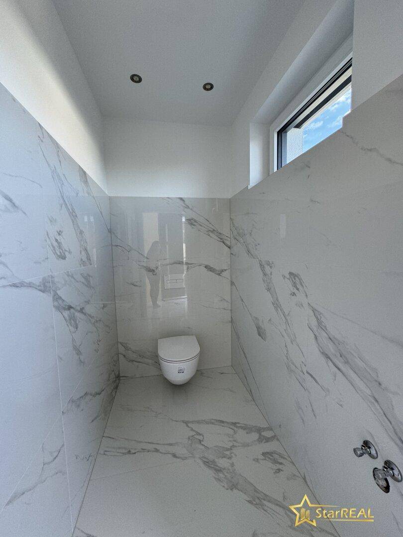 Modernes Gäste-WC mit Marmorfliesen, wandhängendem WC und kleinem Fenster für Tageslicht.