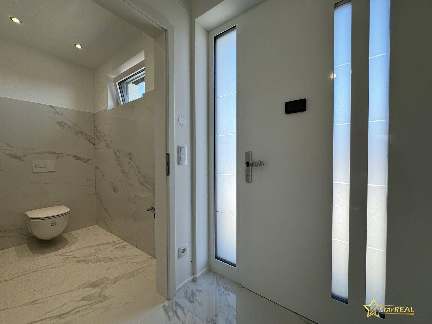 Heller Eingangsbereich mit moderner Haustür und Blick in das stilvolle Gäste-WC.