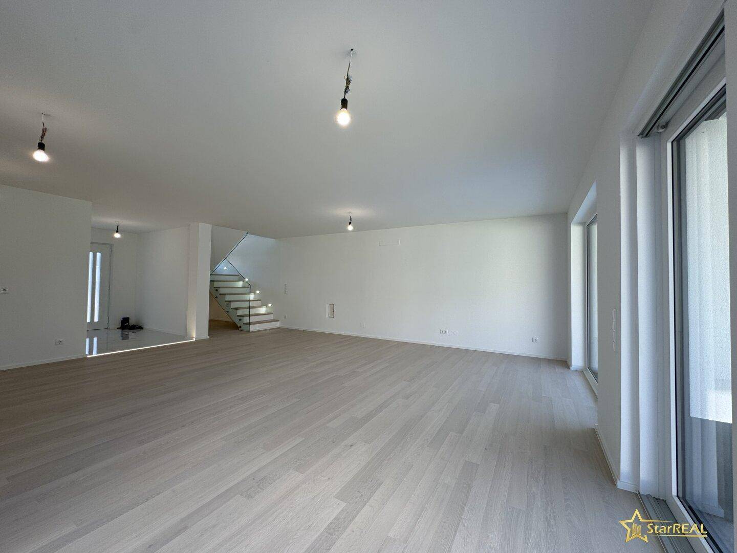 Helles Wohnzimmer mit großen Fensterfronten, die viel Tageslicht hereinlassen und Parkettboden.