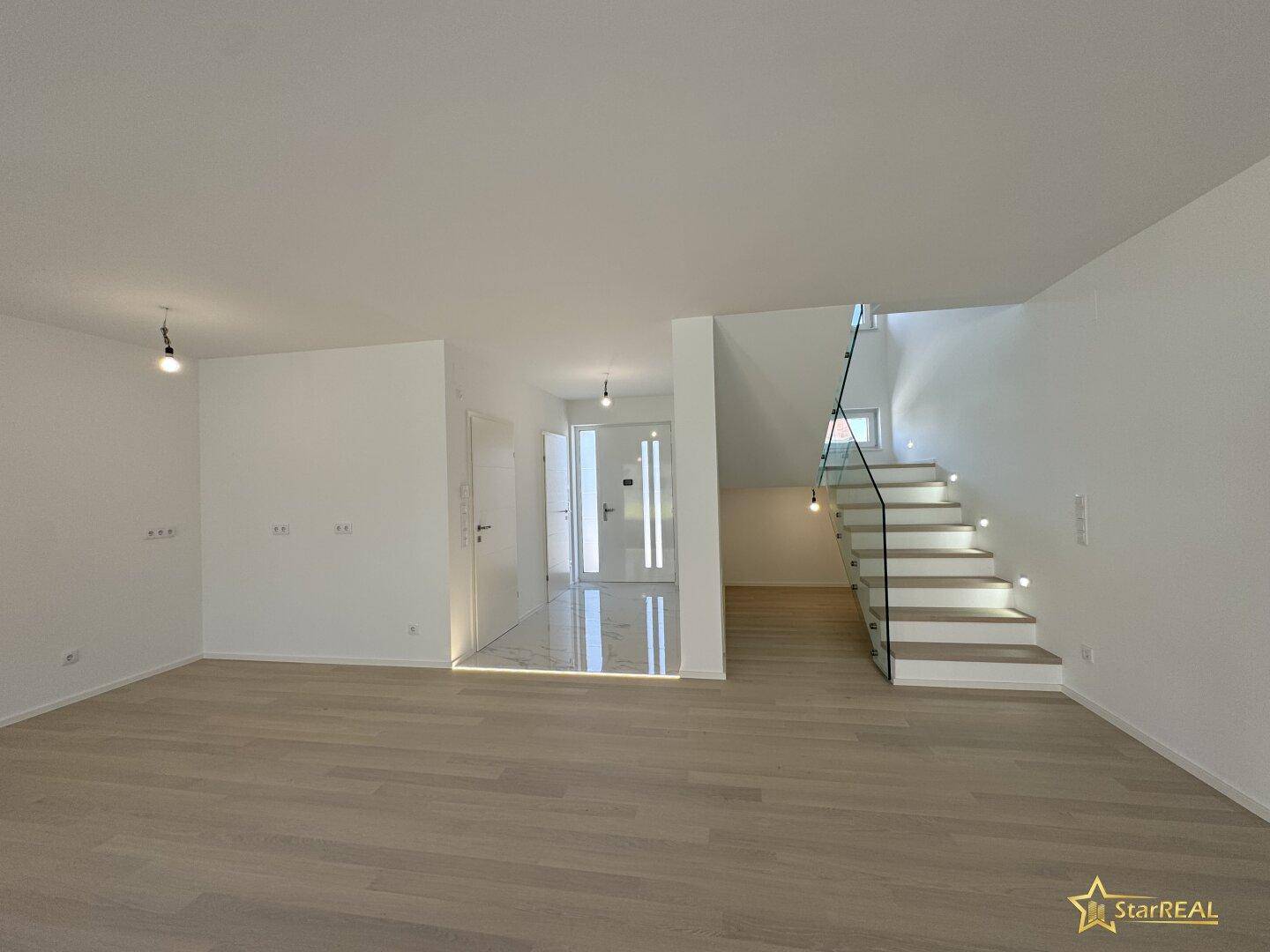 Geräumiger Wohnbereich mit hellem Parkettboden und offenem Übergang zum Eingangsbereich und Treppe.
