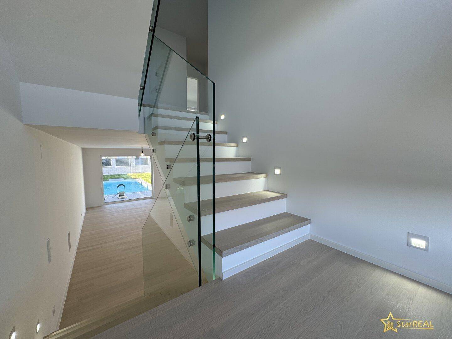Moderne Treppe mit Glasgeländer und beleuchteten Holzstufen, die Eleganz verleiht.