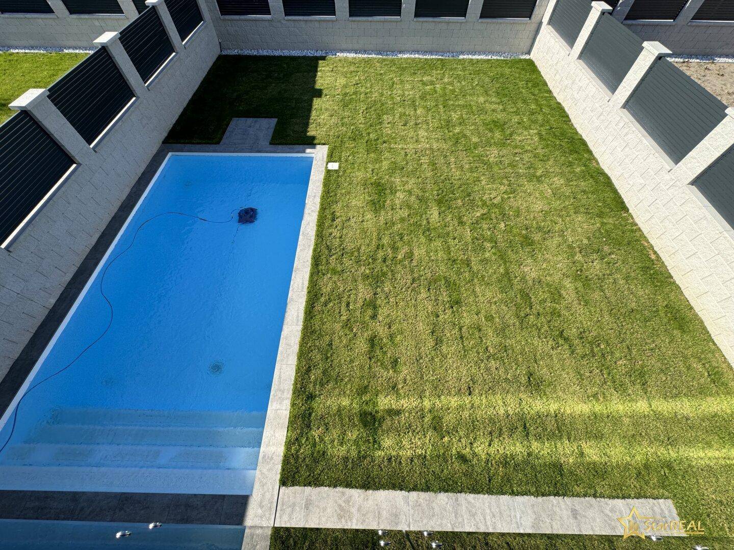 Blick von oben auf den gepflegten Gartenbereich mit rechteckigem Pool und Rasenfläche.