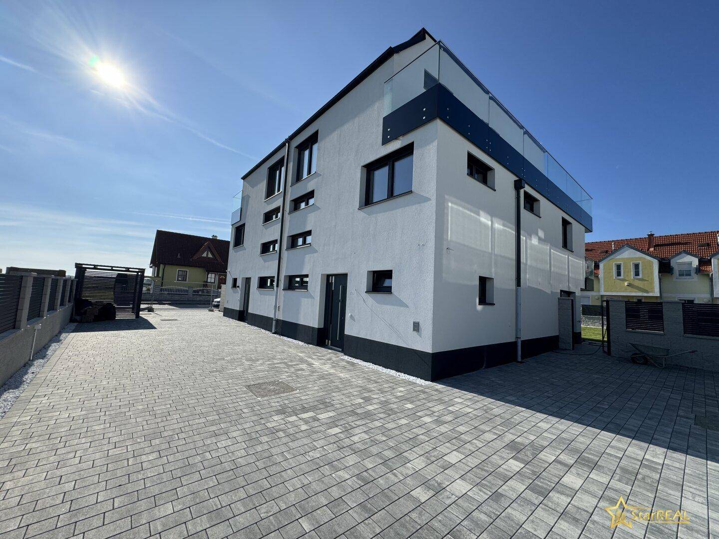 Moderne Fassade des Neubaus mit gepflasterter Einfahrt und klaren architektonischen Linien.