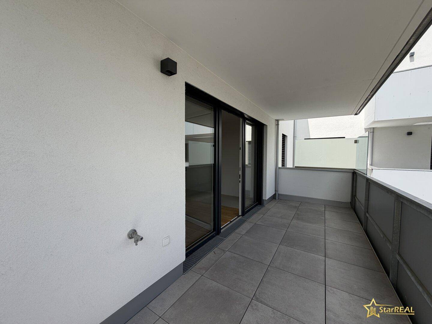 Moderner Balkon mit großen Schiebetüren zum Innenbereich und grauen Bodenfliesen für entspannte Stunden.
