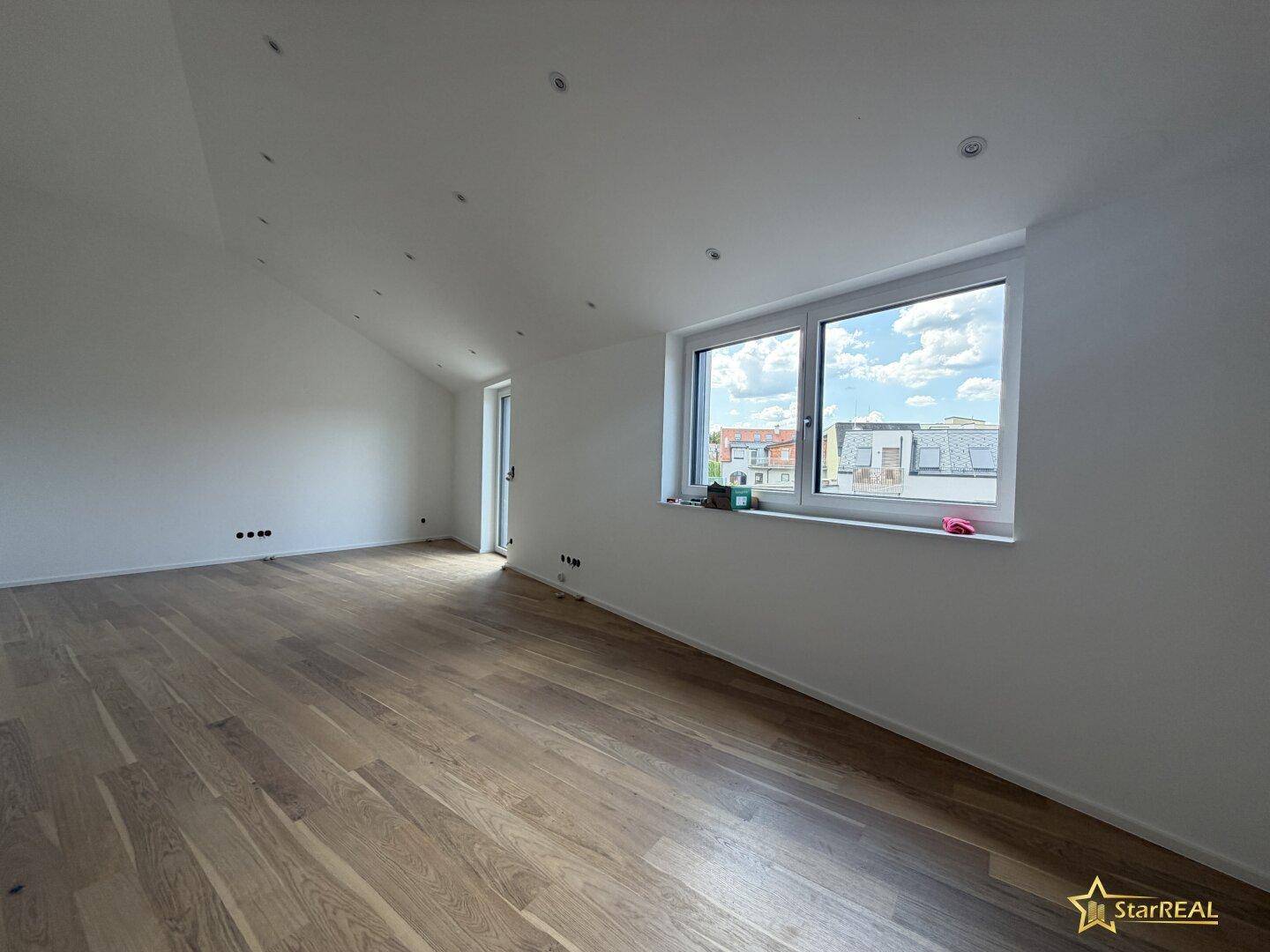 Geräumiger, heller Raum mit Holzboden, weißen Wänden und großem Fenster mit Ausblick.