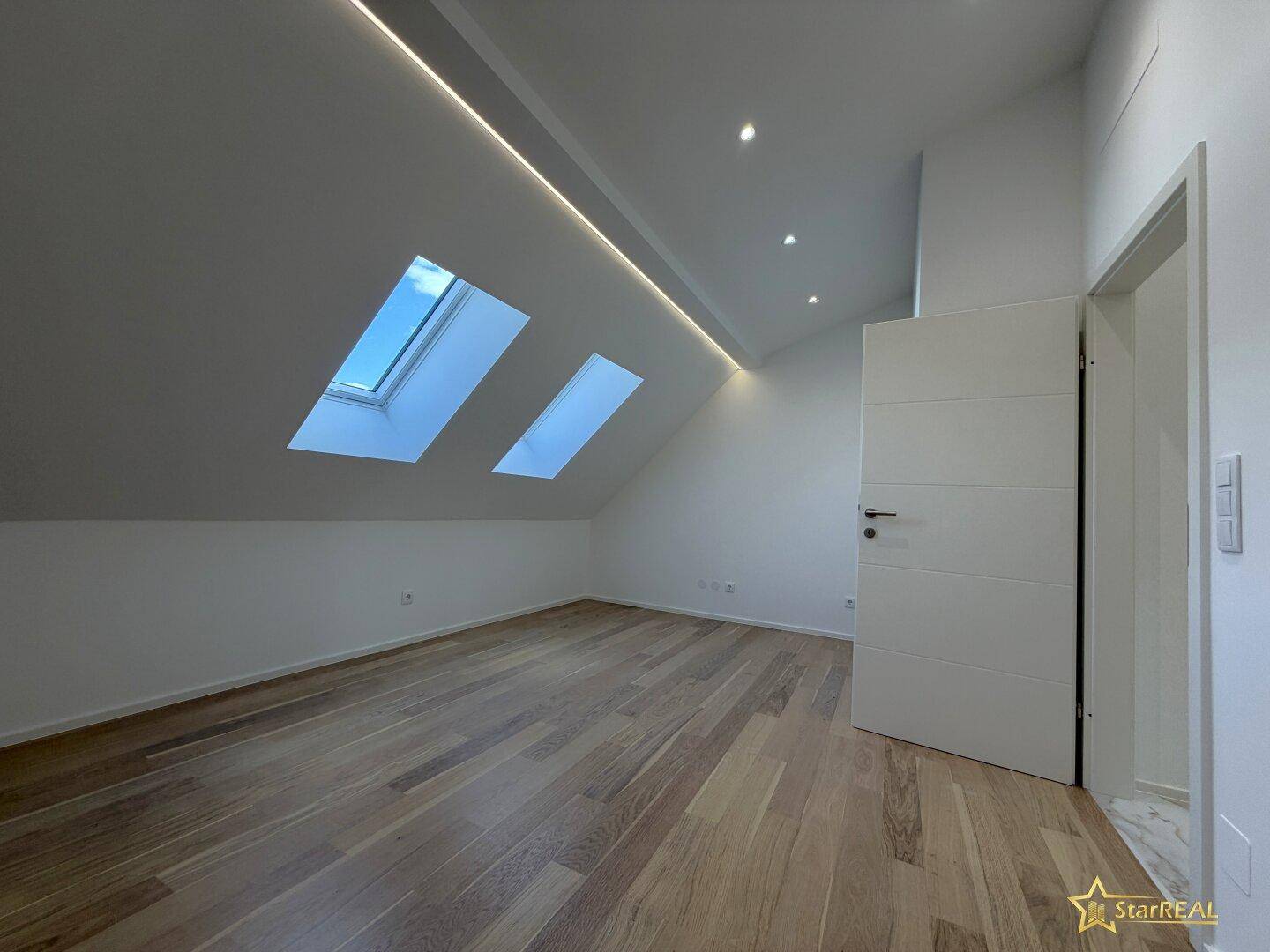 Geräumiger Raum mit Holzboden, Dachschräge und zwei Oberlichtern für viel Tageslicht.