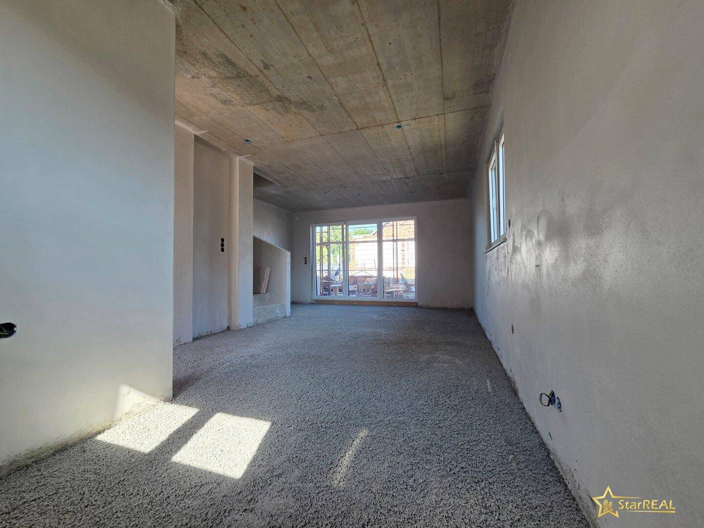 Unfertiger Wohnbereich mit viel Tageslicht und Zugang zu einem möglichen Außenbereich.