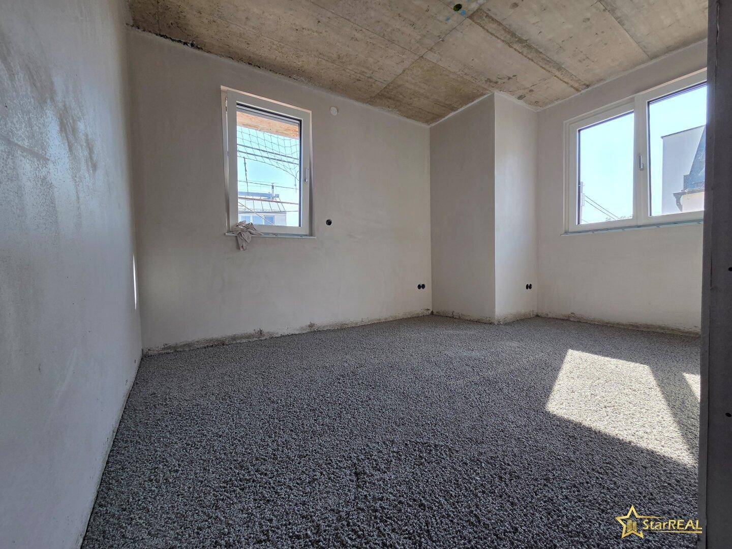 Helles Schlafzimmer im Rohbau mit zwei Fenstern und Estrichboden, viel Tageslicht.