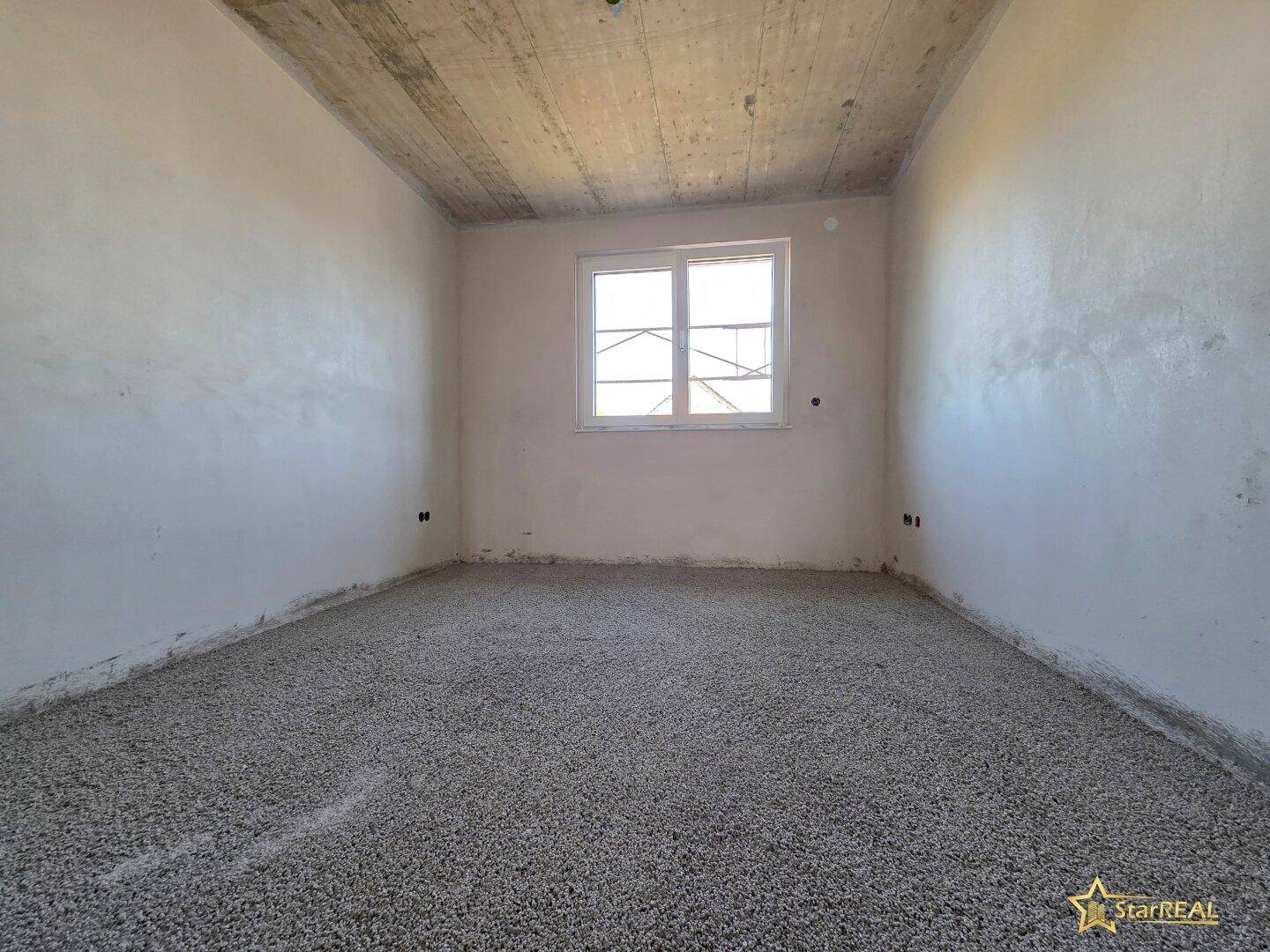 Heller Raum im Rohbau mit einem Fenster und Estrichboden, ideal als Schlafzimmer.