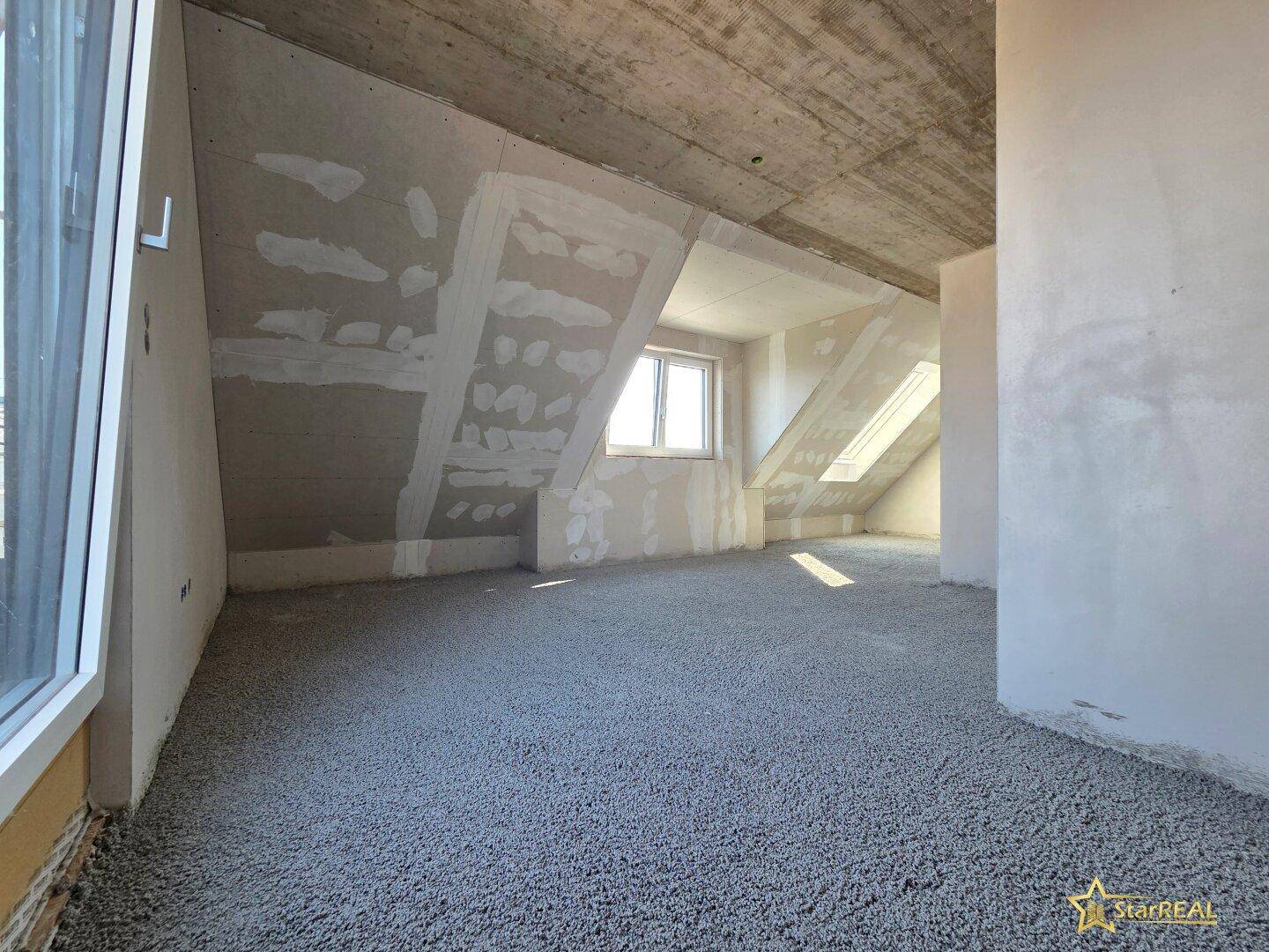 Dachgeschossraum im Rohbau mit schrägen Wänden, Fenster und Dachfenster für mehr Licht.