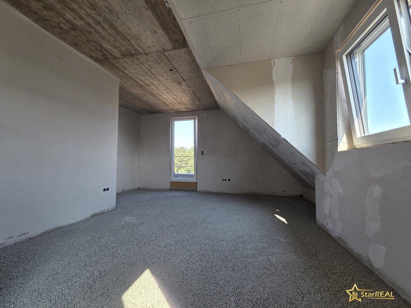 Dachgeschossraum im Rohbau mit Zugang zum Außenbereich und Fenster, viel natürliches Licht.