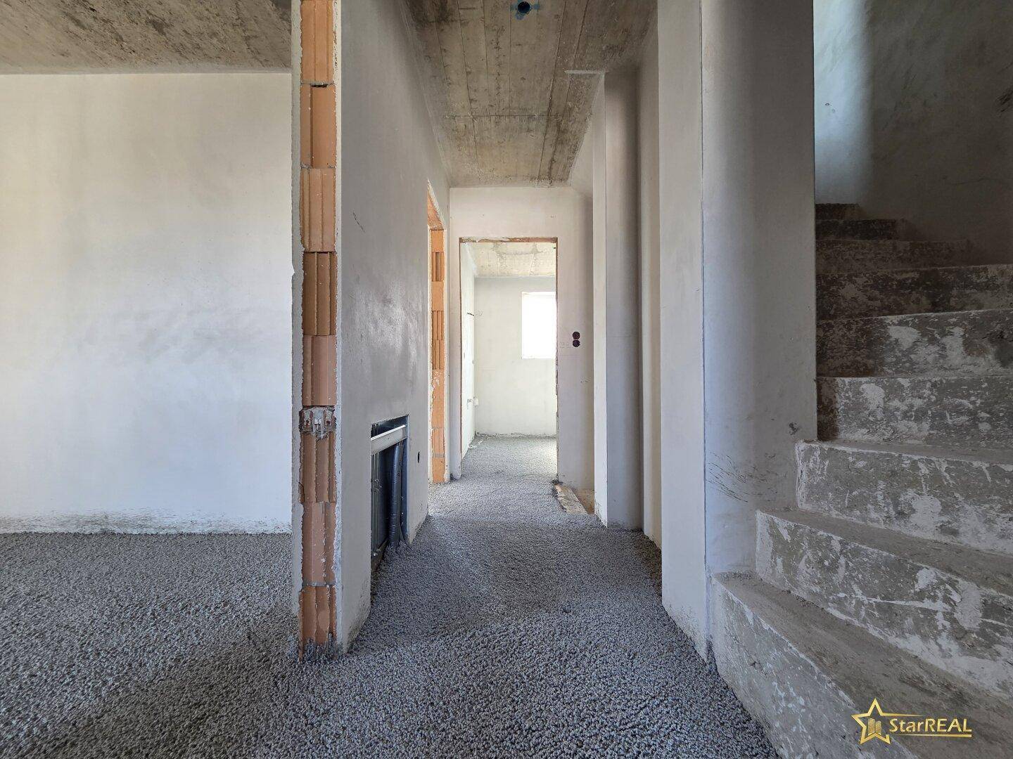 Flurbereich im Rohbau mit Treppenaufgang und Zugang zu weiteren Räumen.