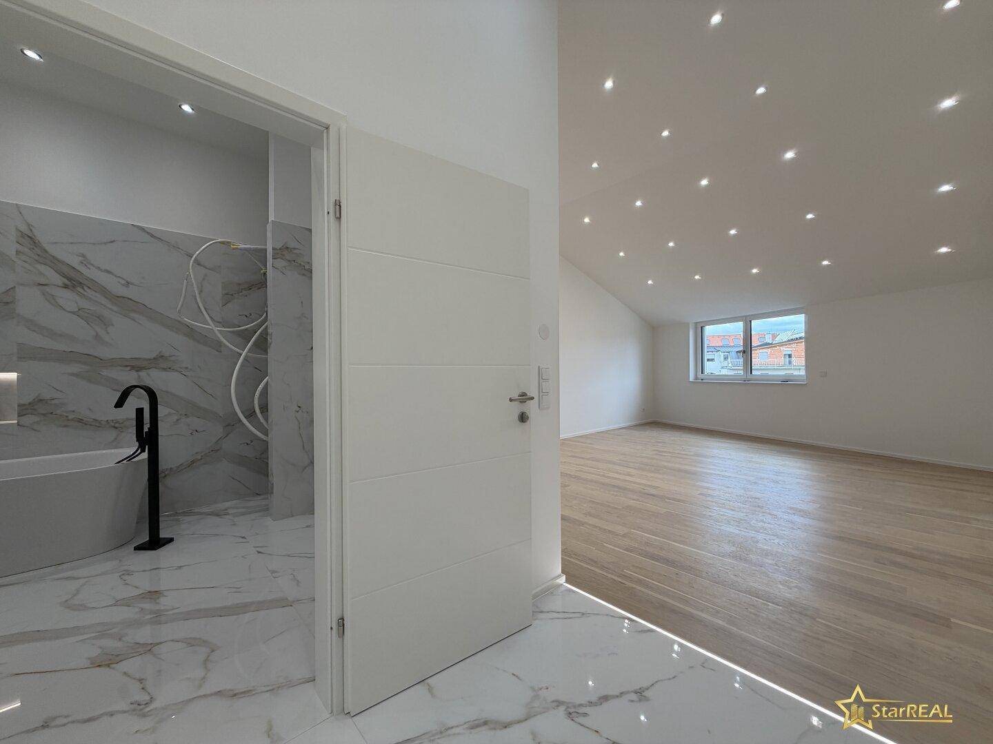 Modernes Badezimmer mit Marmorfliesen und freistehender Badewanne, angrenzend an einen Raum mit Parkettboden.