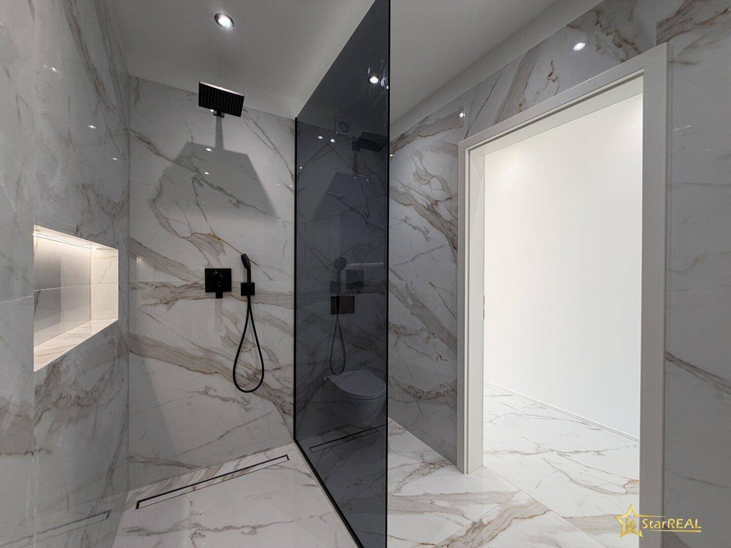 Modernes Badezimmer mit großformatigen Marmorfliesen und einer begehbaren Dusche mit schwarzer Armatur.
