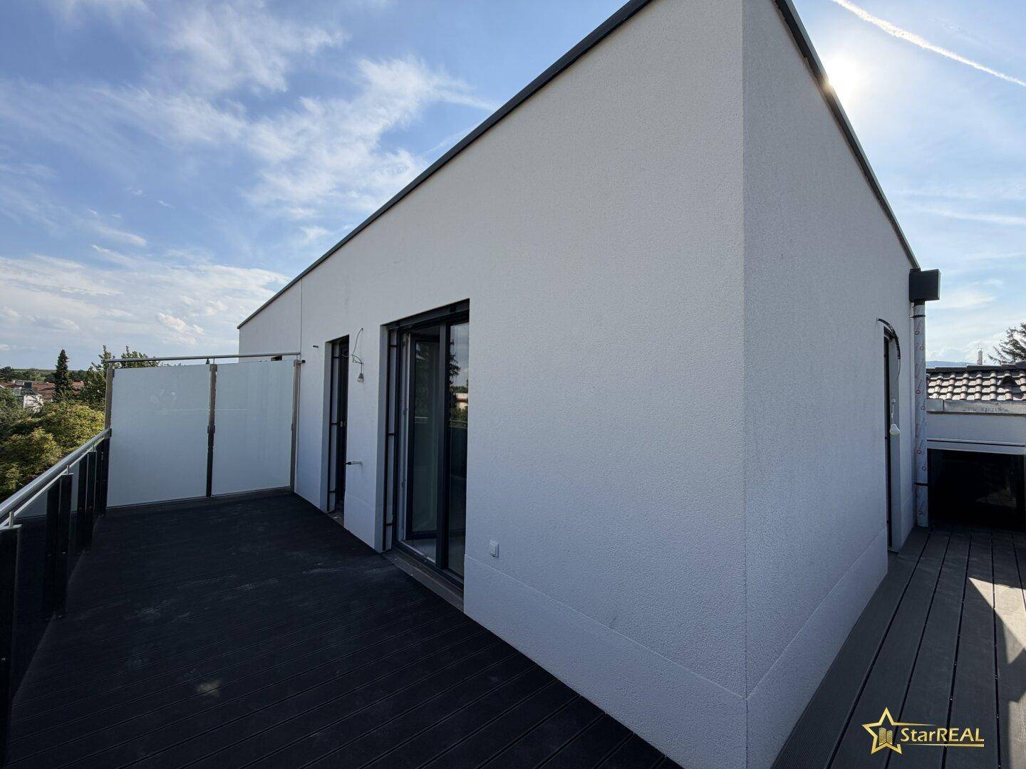 Großer Balkon mit dunklem Bodenbelag und Glasgeländer, ideal für entspannte Stunden im Freien.