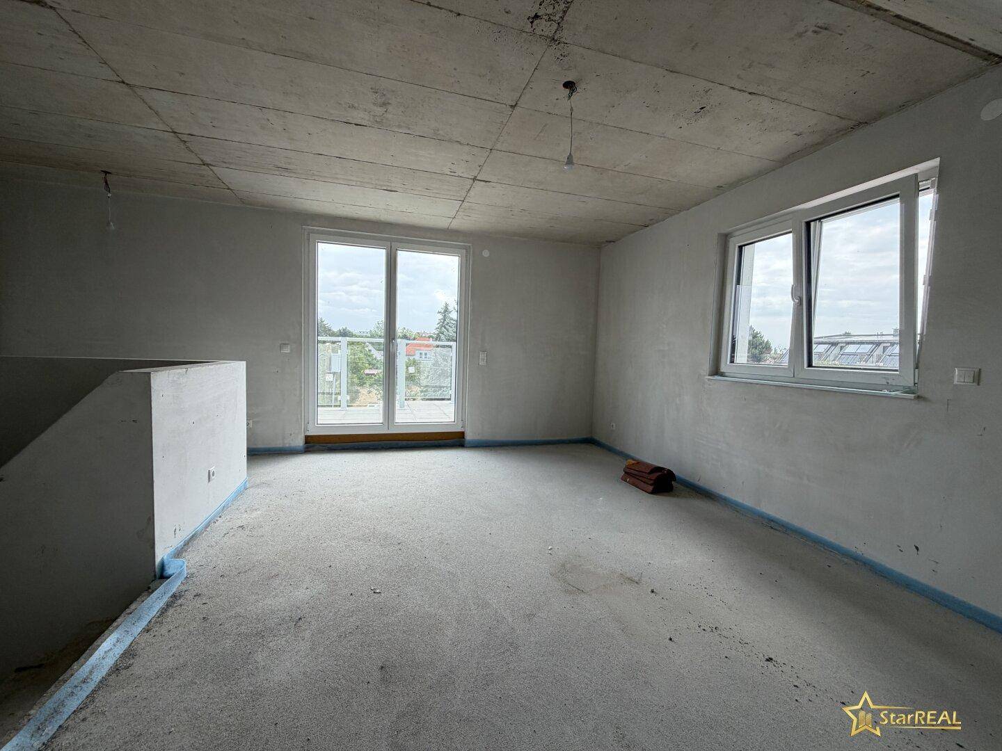 Unfertiger Innenraum mit Betonboden und großen Fenstern, bereit für den Ausbau.