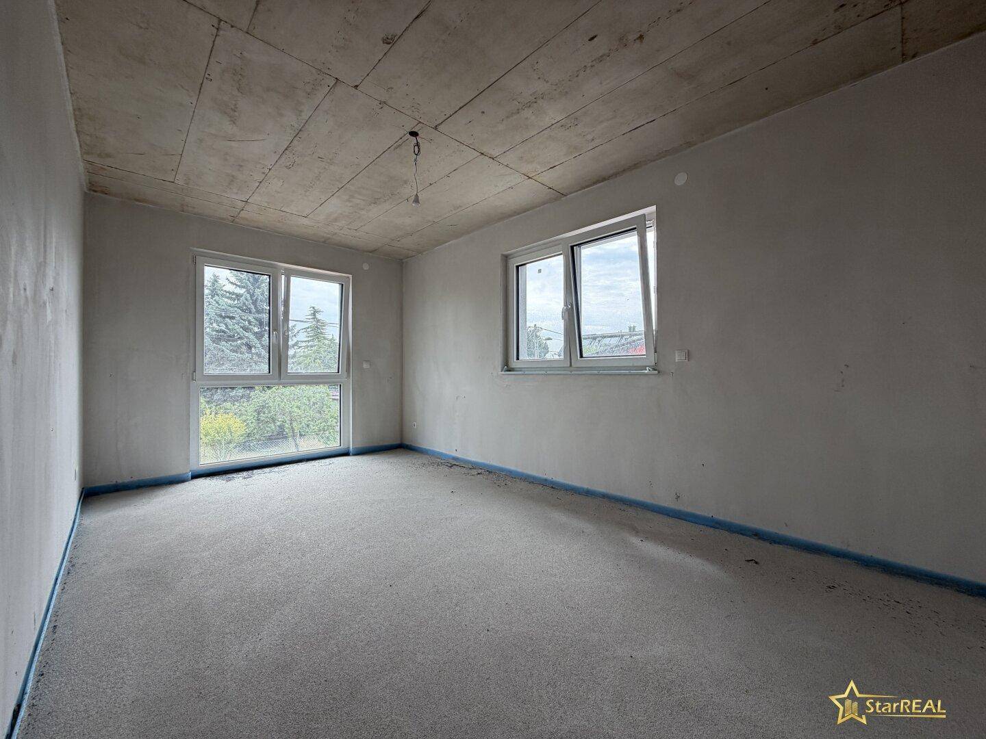 Heller, unmöblierter Raum im Rohbauzustand mit zwei Fenstern und Betonoberflächen.