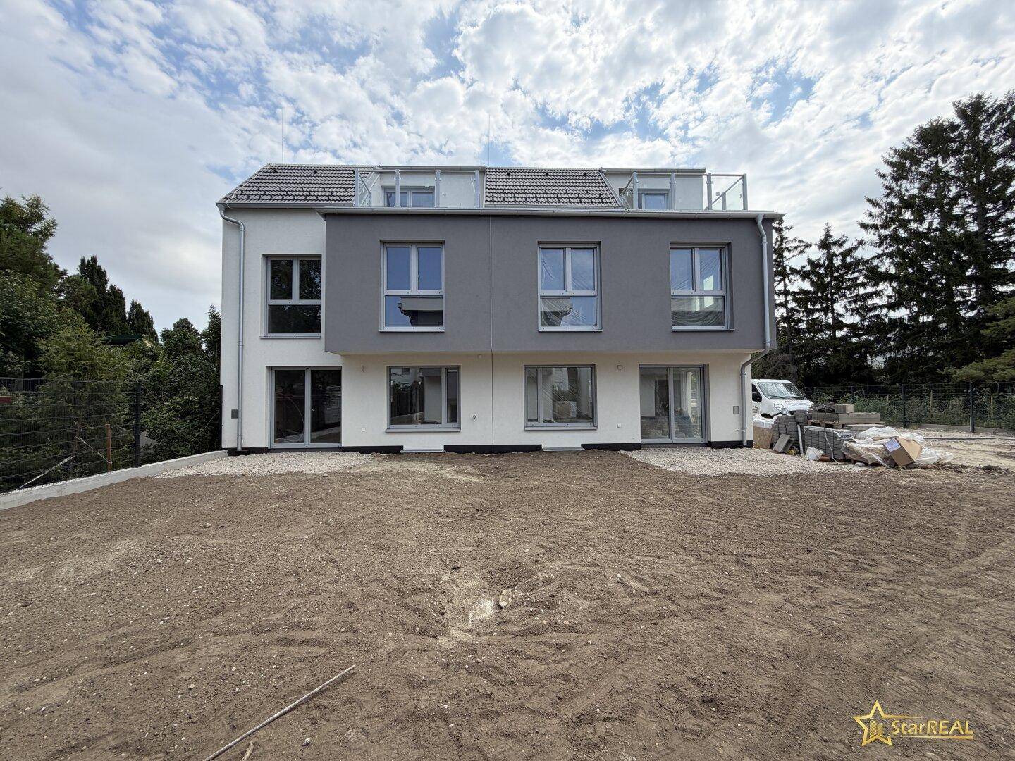 Rückansicht einer Reihe von modernen Neubauten mit Terrassenzugang und Gartenbereich.