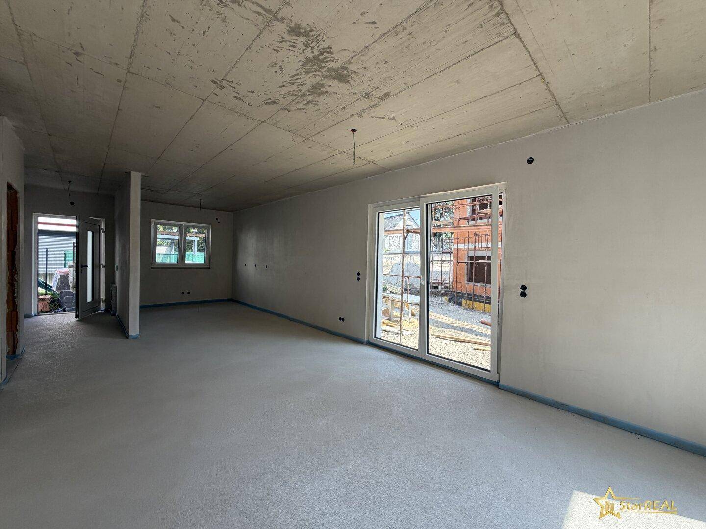 Heller Wohnraum im Rohbau mit großen Schiebetüren und Blick auf die Baustelle.