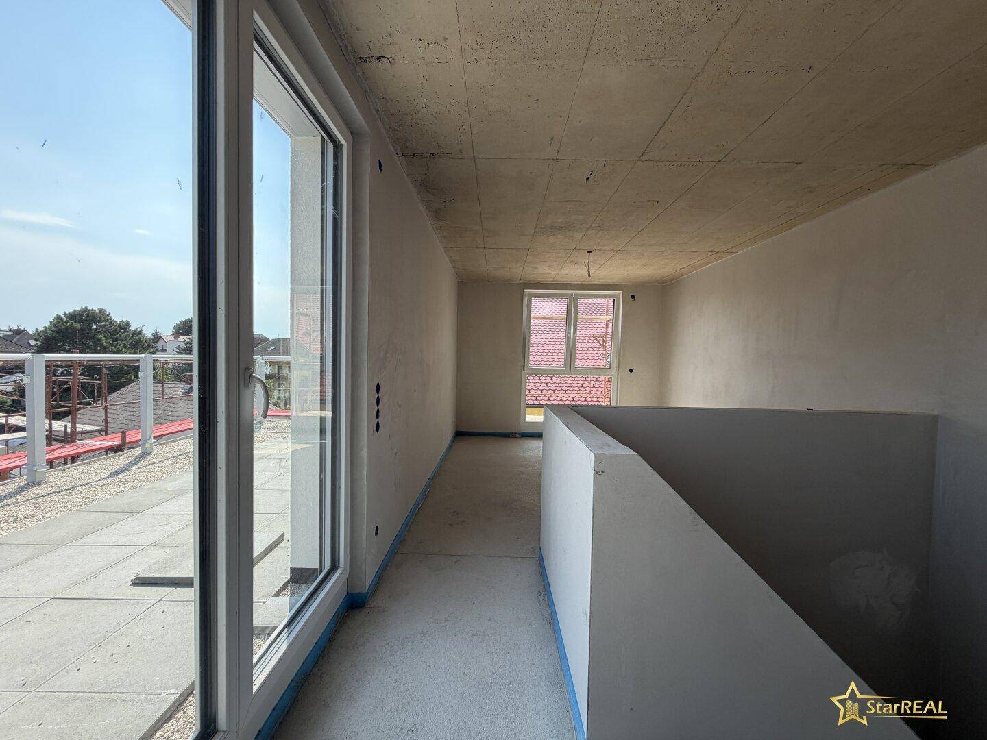 Heller Flur im Rohbau mit großen Glasfronten und Zugang zur Terrasse.