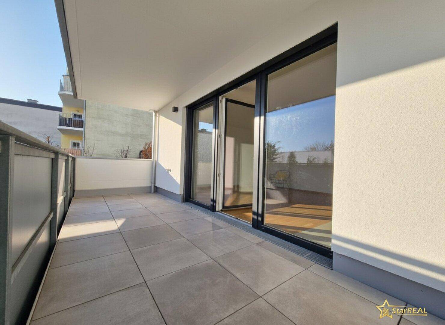 Geräumiger Balkon mit modernen Fliesen, großen Glasfronten und viel Sonnenlicht.