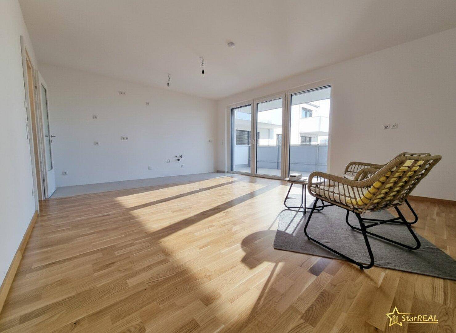 Heller Wohnraum mit hochwertigem Parkettboden, großen Schiebetüren und Zugang zu einem Balkon.