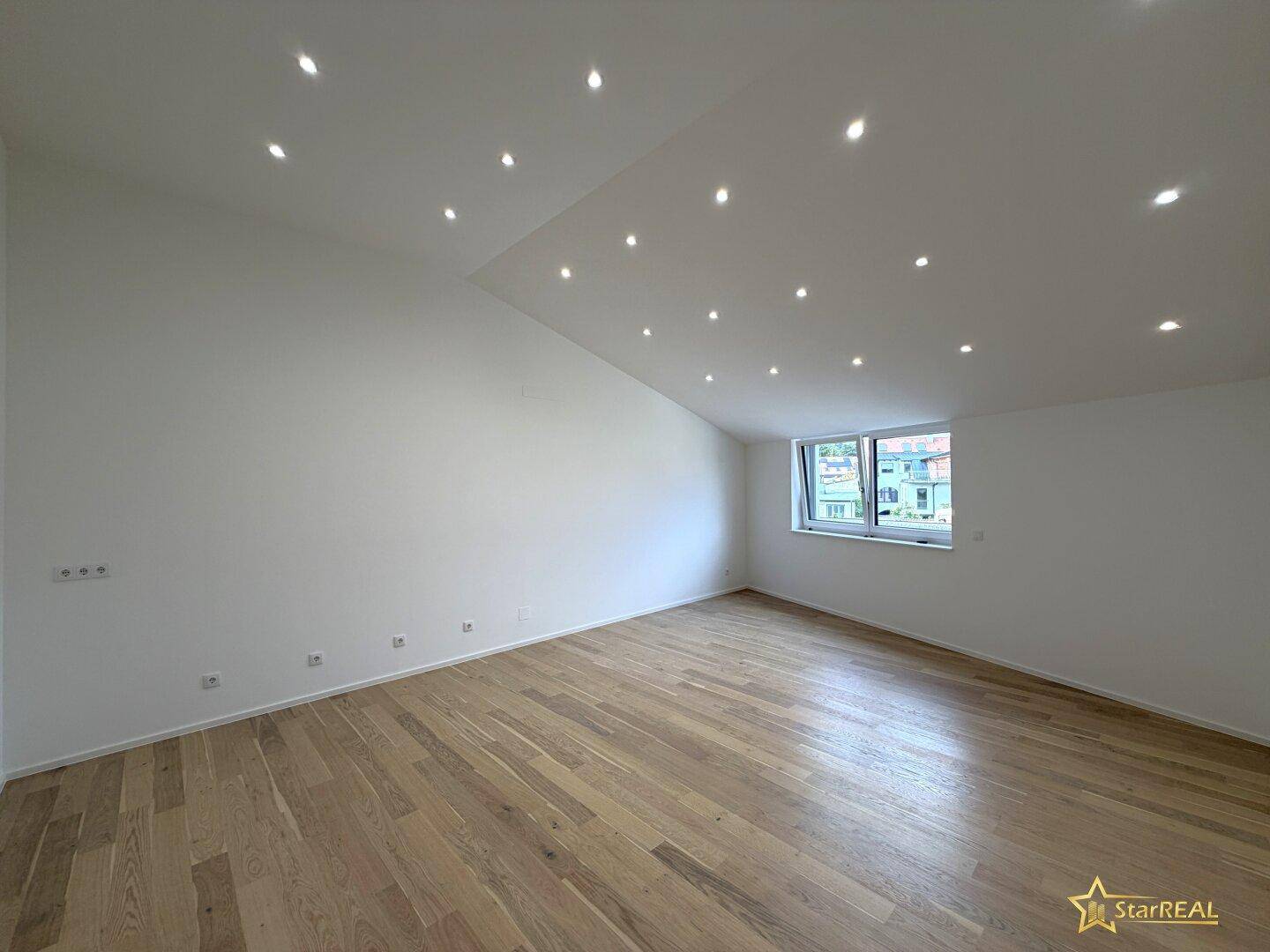 Geräumiger, heller Raum mit Holzboden, vielen Deckenspots und schrägen Wänden im Dachgeschoss.