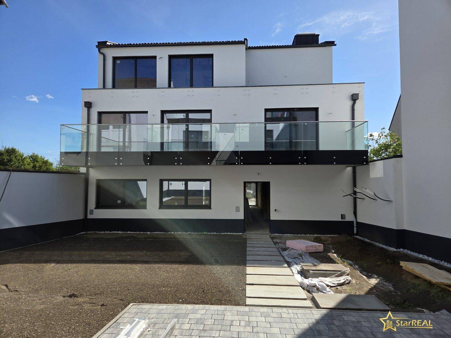 Rückseite eines modernen Neubaus mit Terrassen, Balkonen und einem vorbereiteten Gartenbereich.