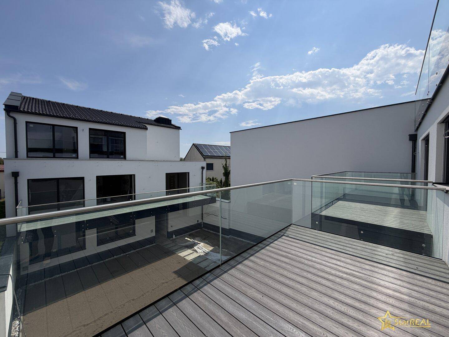 Großer Balkon mit Holzdielen und Glasgeländer, bietet einen weiten Blick auf die Umgebung.