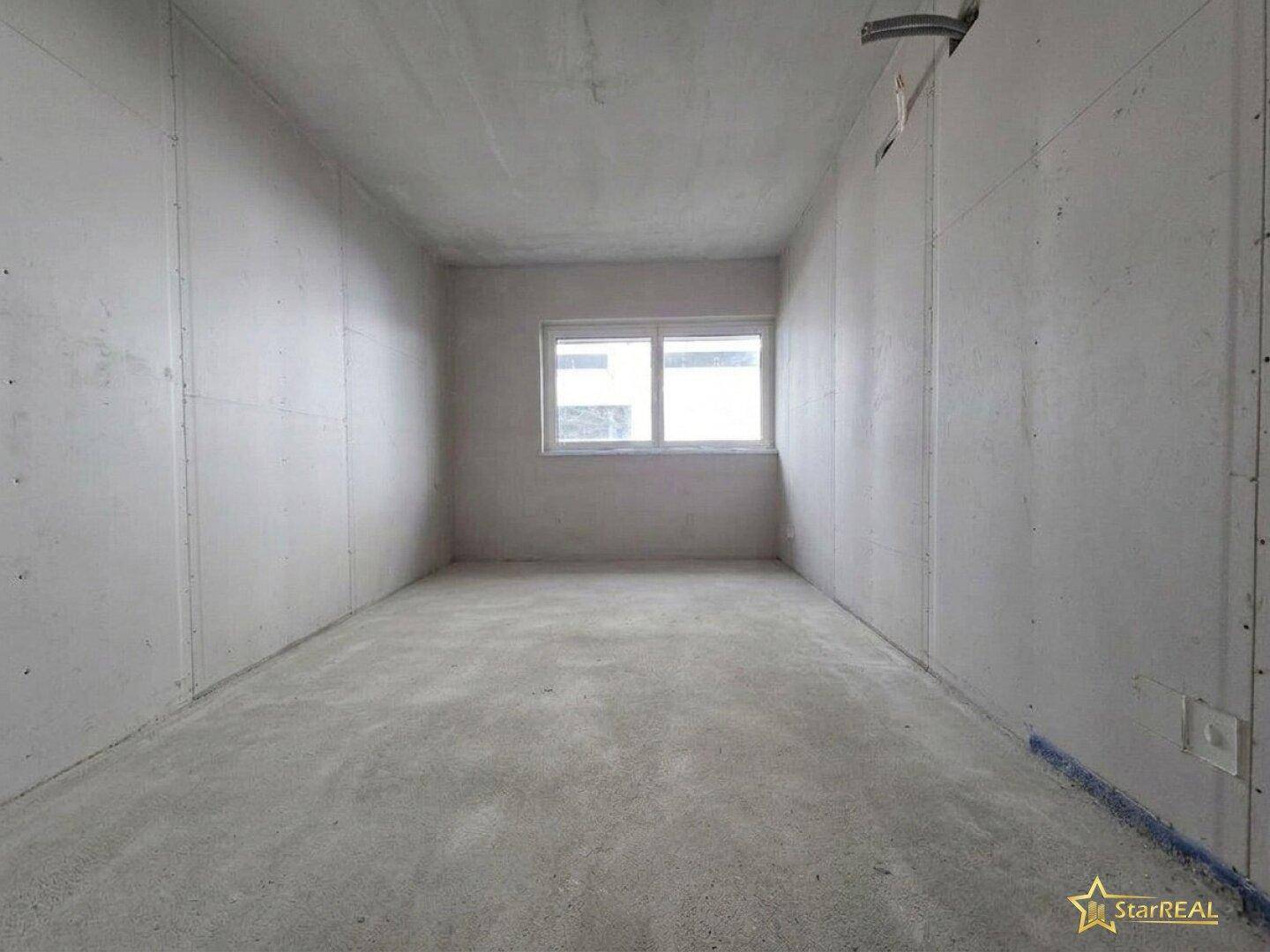 Unfertiger Raum im Rohbauzustand mit Betonboden und Fenster, bereit für den Ausbau.