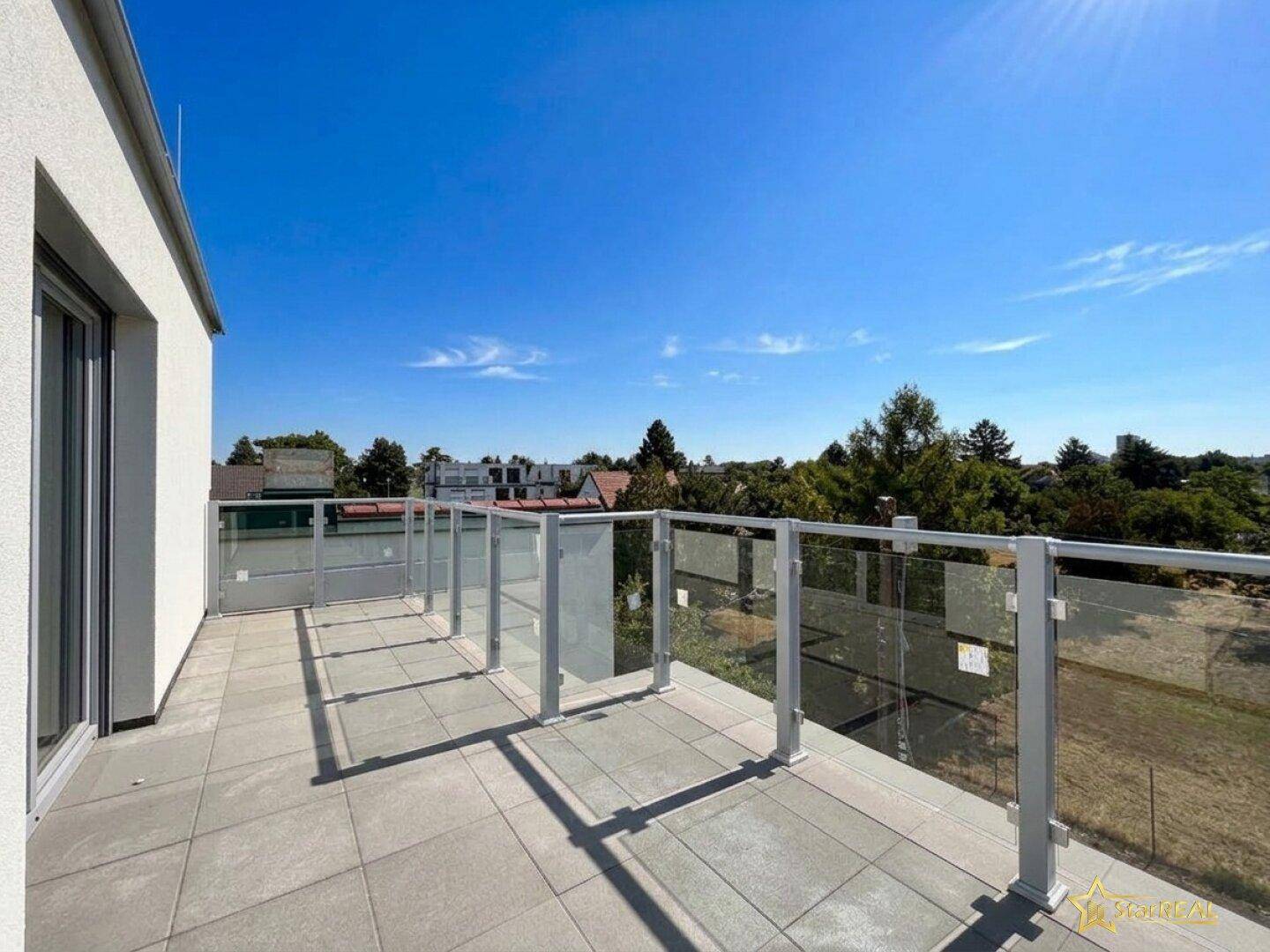 Geräumige Dachterrasse mit Fliesenboden und Glasgeländer bietet weite Aussicht.