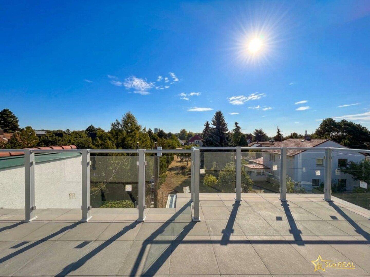 Sonnige Dachterrasse mit modernem Glasgeländer und Blick auf die Umgebung.