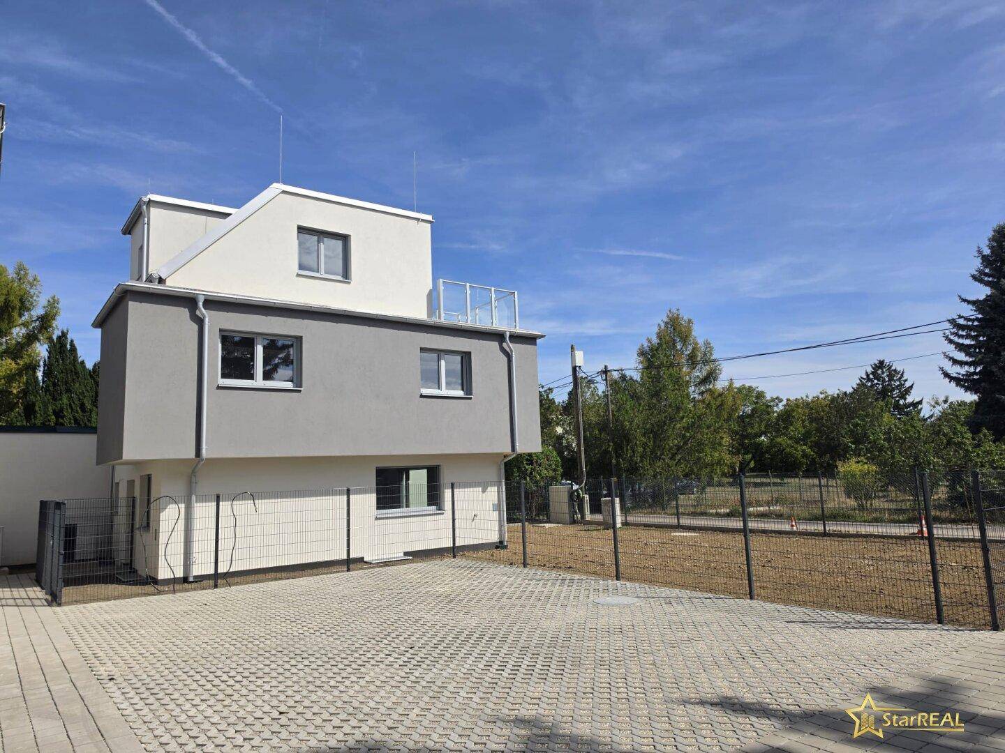 Neubau mit moderner Architektur, grauer Fassade und gepflastertem Außenbereich.