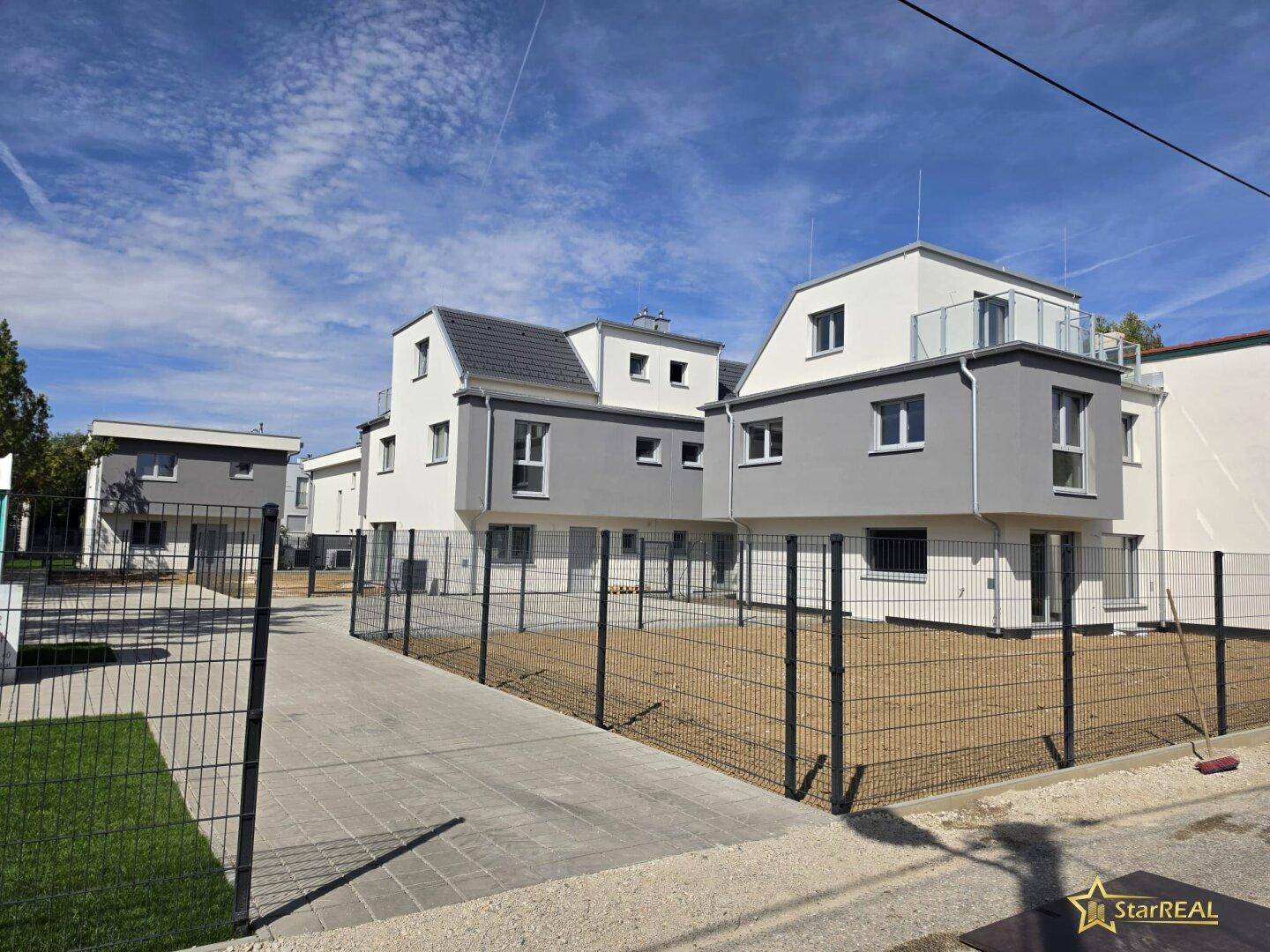 Mehrere moderne Neubauten mit grauen und weißen Fassaden in einer Wohnsiedlung.