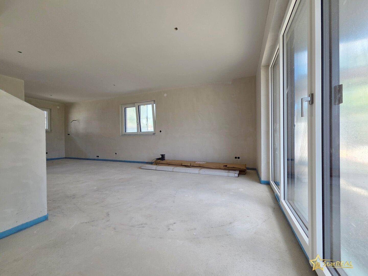 Heller Wohnbereich im Rohbau mit großen Fensterfronten, die viel Licht hereinlassen.